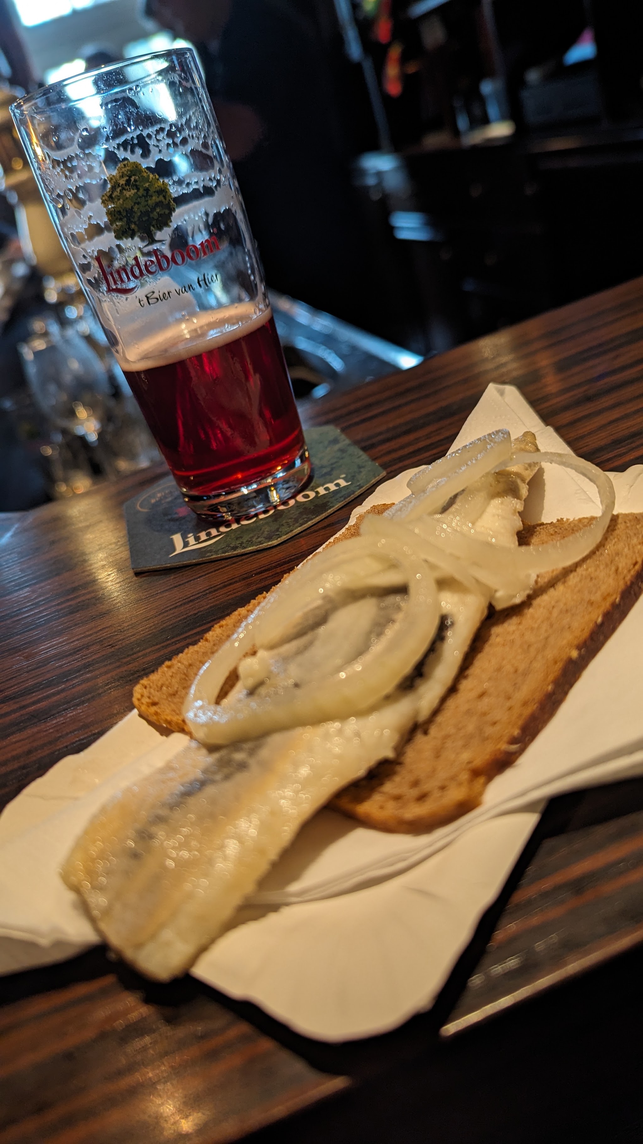 Haring op roggebrood met ui naast een glas Lindeboom op de bar